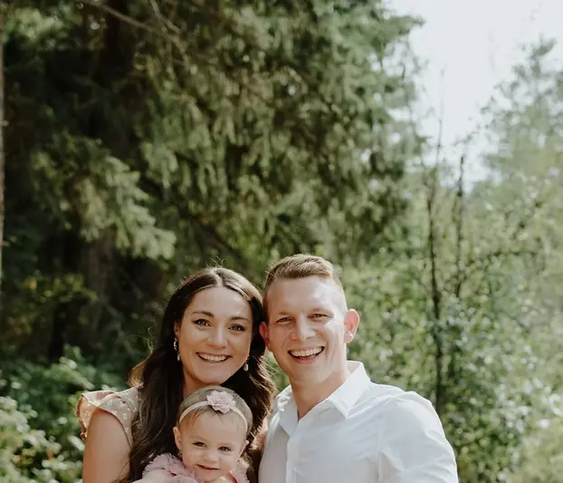 A man, woman, and young child pose together outdoors in front of trees, smiling at the camera—perhaps celebrating a successful septic system installation Michigan recently completed for their home. Kenneth Bros